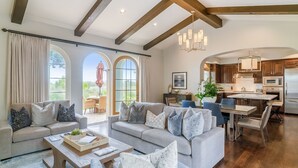 A spacious living room with a sofa, coffee table, and dining area with chairs. A kitchen with modern appliances is visible in the background. - 3 Bedroom Ocean Villa (Rancho Palos Verdes)
