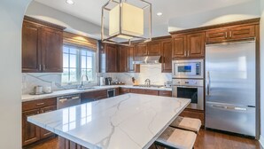 A modern kitchen with marble countertops, stainless steel appliances, and wooden cabinetry. - 3 Bedroom Ocean Villa (Rancho Palos Verdes)