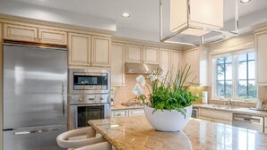 A modern kitchen with stainless steel appliances, a granite countertop, and a large island with bar stools. - 3 Bedroom Resort Villa (Rancho Palos Verdes)