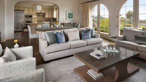 A spacious living room with a grey sofa, a glass coffee table, and a view of the kitchen and outdoor patio. - 3 Bedroom Resort Villa (Rancho Palos Verdes)