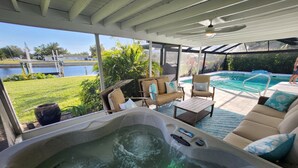 A hot tub with a view of a swimming pool and a grassy area.