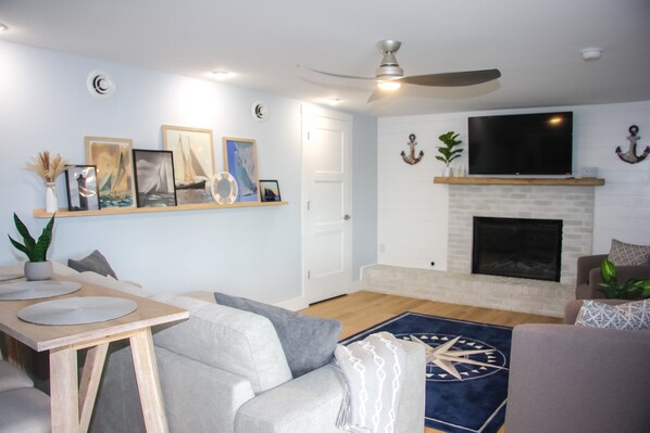 A living room with a fireplace, a flat-screen TV, and a ceiling fan.