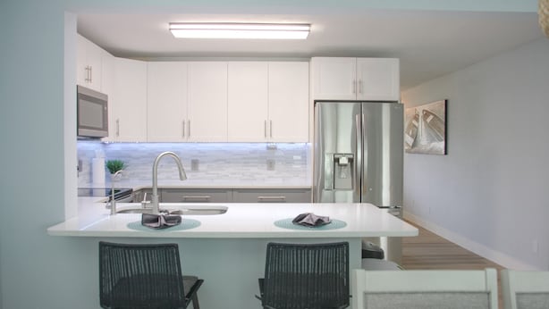 A modern kitchen with white cabinets, a stainless steel refrigerator, and a built-in island with two bar stools.