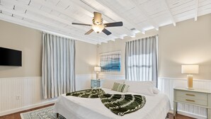 A bedroom with a bed, a ceiling fan, a mounted TV, a nightstand, a lamp, and a painting on the wall. - America's Lake Cabin with Patio & Firepit! (Nevada)