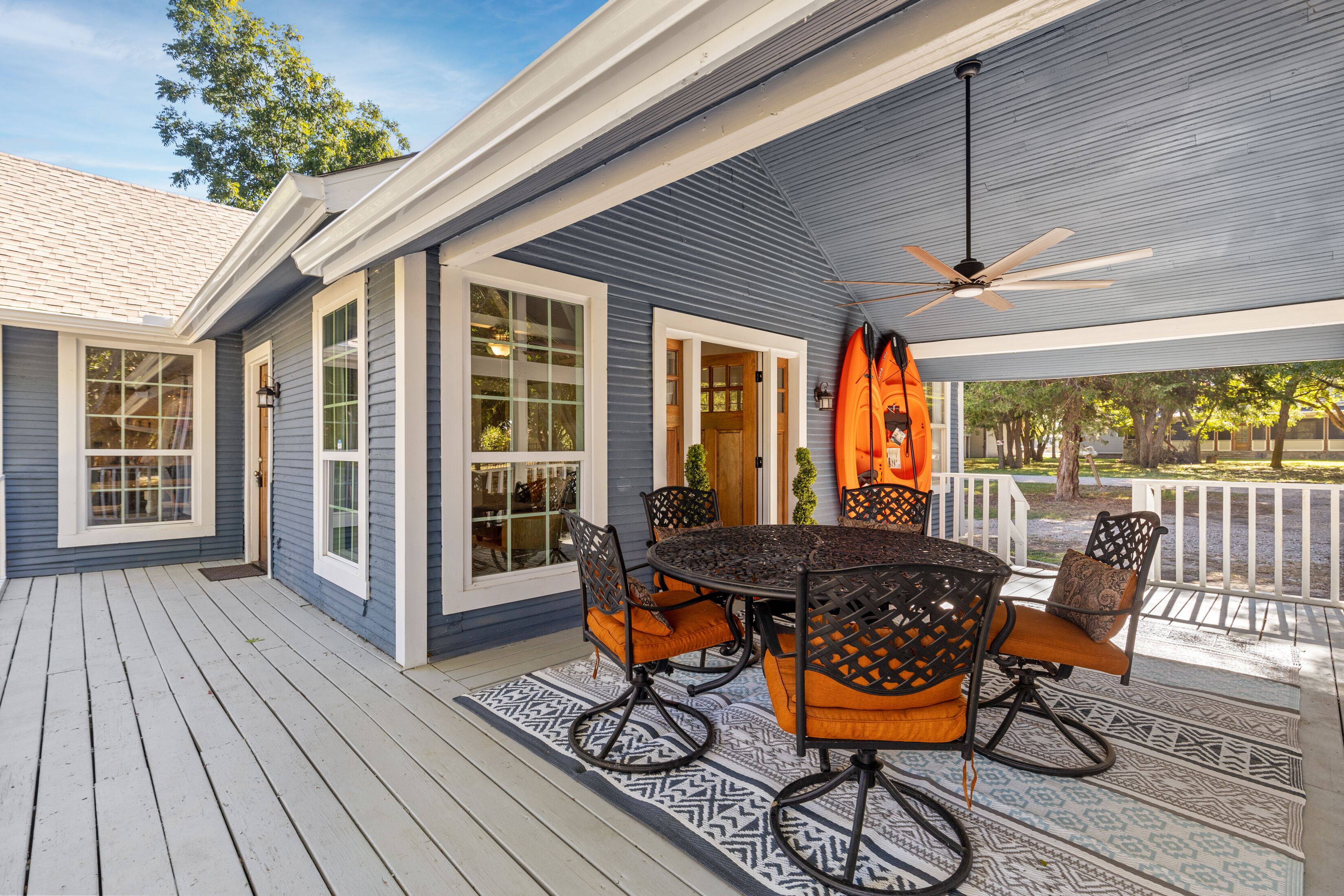 A covered outdoor patio with a round table and chairs, a ceiling fan, and a view of the surrounding area.