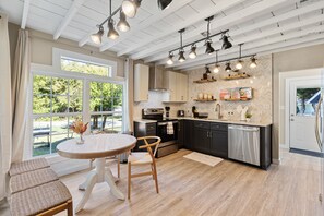 Une cuisine moderne dotée d’un grand îlot central, de luminaires suspendus et offrant une vue sur l’extérieur.