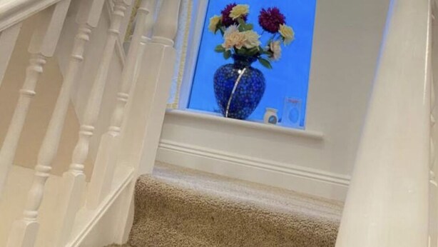 A staircase with white balusters and a blue vase with flowers on the landing. - Valentia Skellig Rooms (Valentia Island)