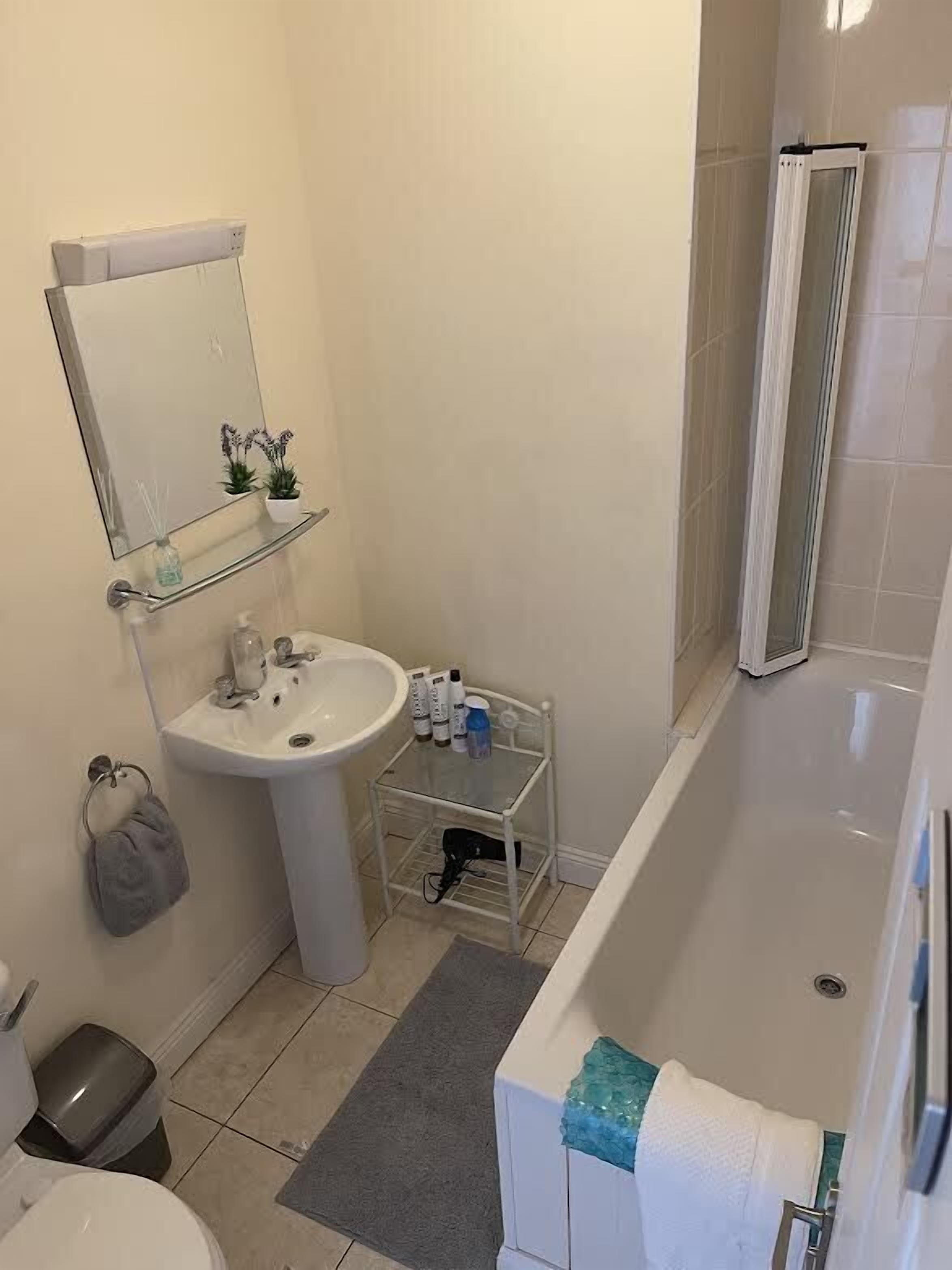 A bathroom with a sink, mirror, towel rack, shower, and a small shelf with toiletries.