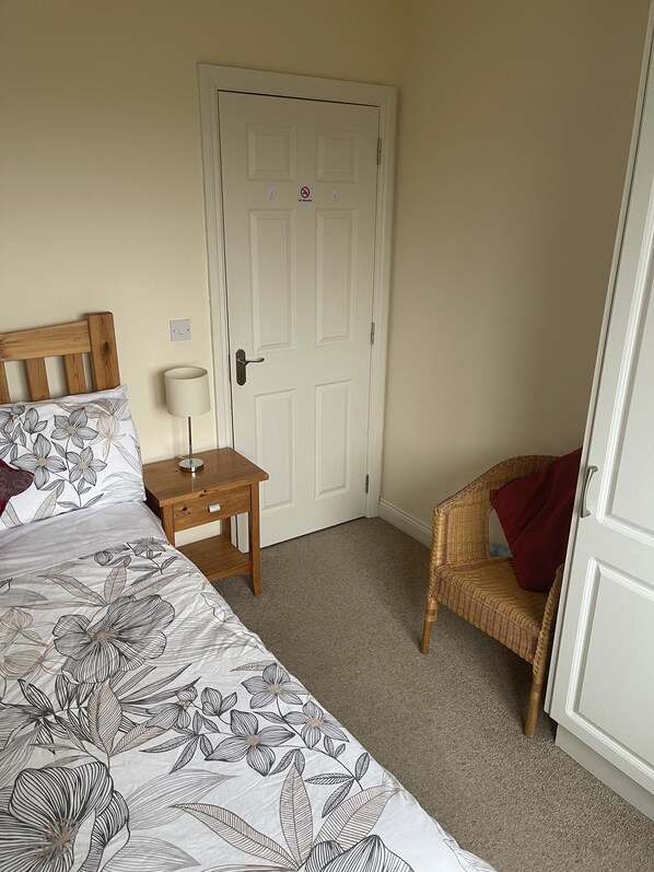 A bedroom with a bed, bedside table, lamp, chair, and a door with a "No Smoking" sign. - Valentia Skellig Rooms (Valentia Island)