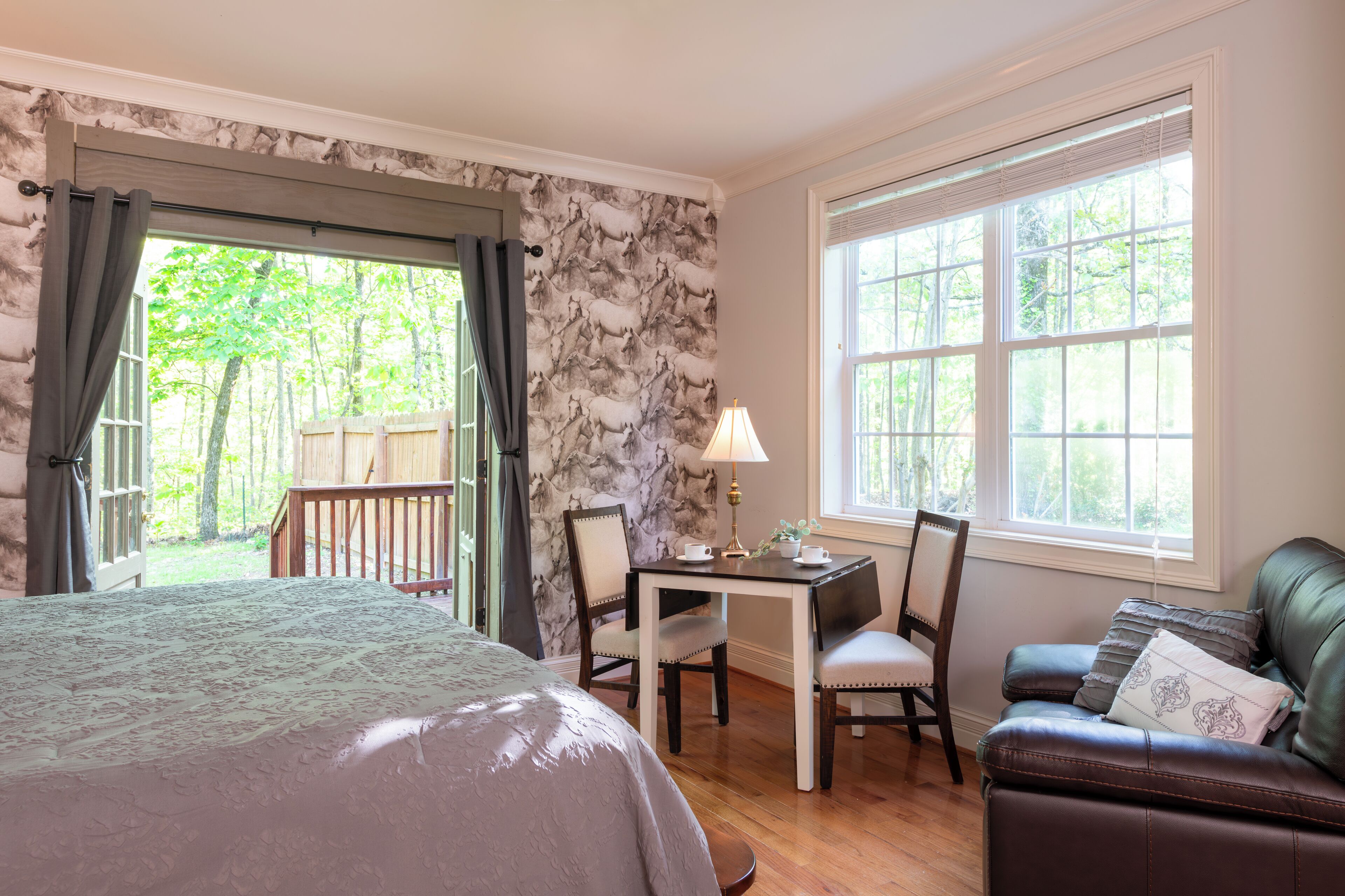 Ein Schlafzimmer mit einem großen Bett, einem Schreibtisch mit Stuhl, einem Ledersofa und einem Fenster mit Blick auf Bäume.