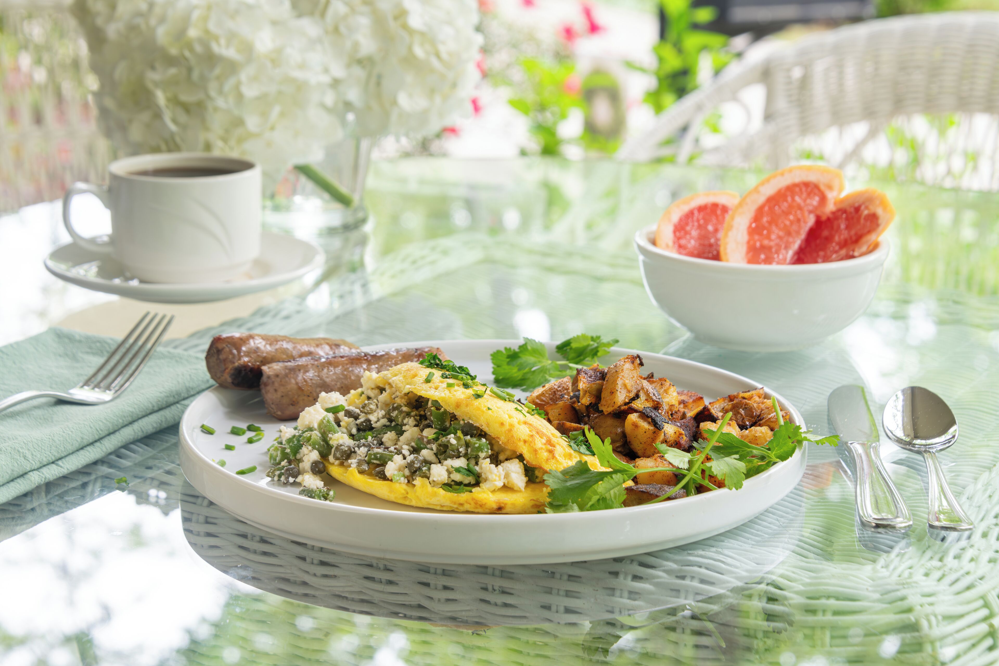 A breakfast setting with a plate of food, a cup of coffee, and a bowl of fruit.