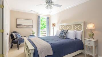 A bedroom with a bed, a chair, a nightstand, a ceiling fan, and a window with curtains.
