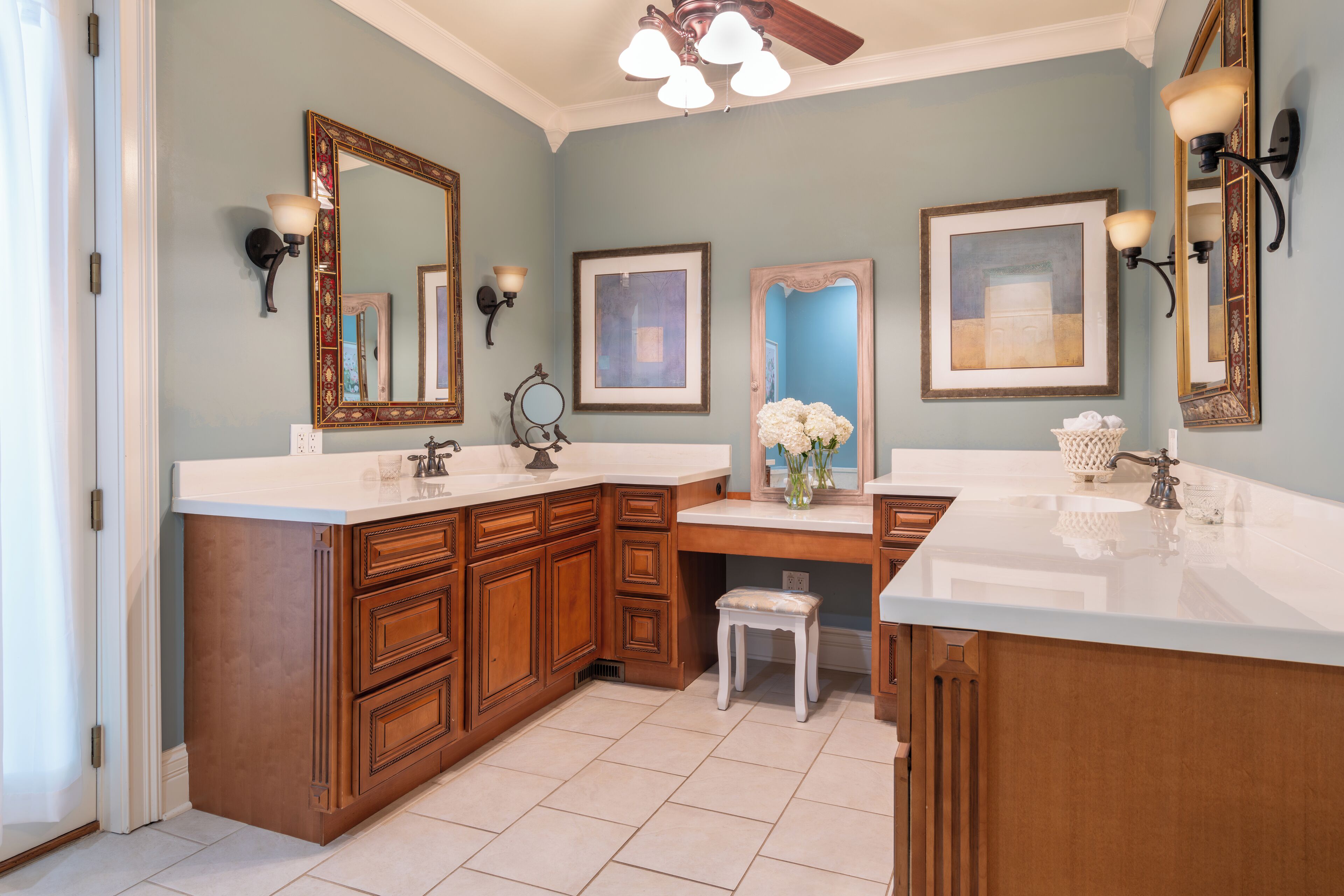 A bathroom with two sinks, wooden cabinetry, and a vanity with a stool.