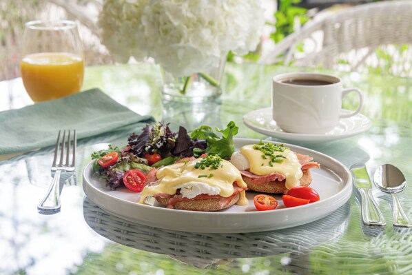 A breakfast setting with a plate of eggs benedict, a glass of orange juice, and a cup of coffee on a table with a green tablecloth. - The Sage Cottage (Adairsville)