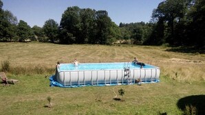 Piscina rectangular elevada con una escalera en un lateral, rodeada de un campo cubierto de césped y árboles al fondo.