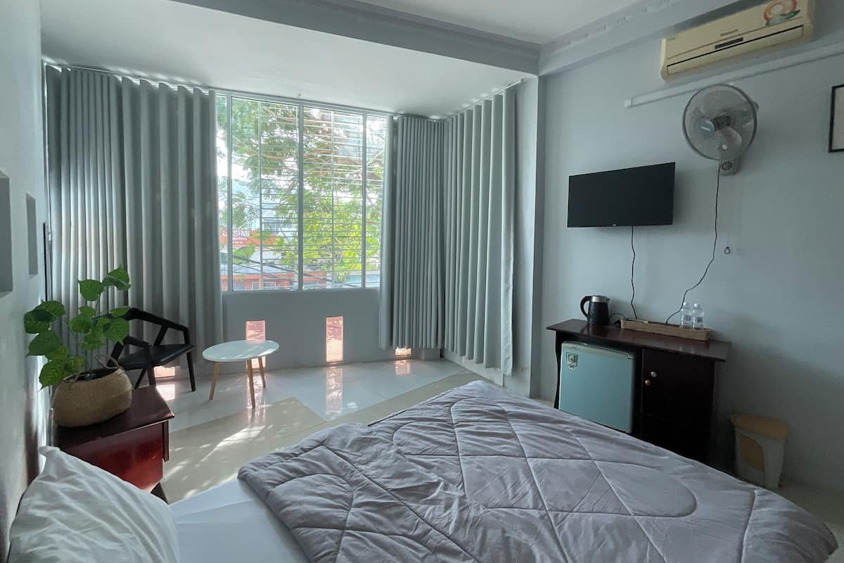 A modern hotel room with a large bed, a desk with a computer, a TV mounted on the wall, and a window with curtains.