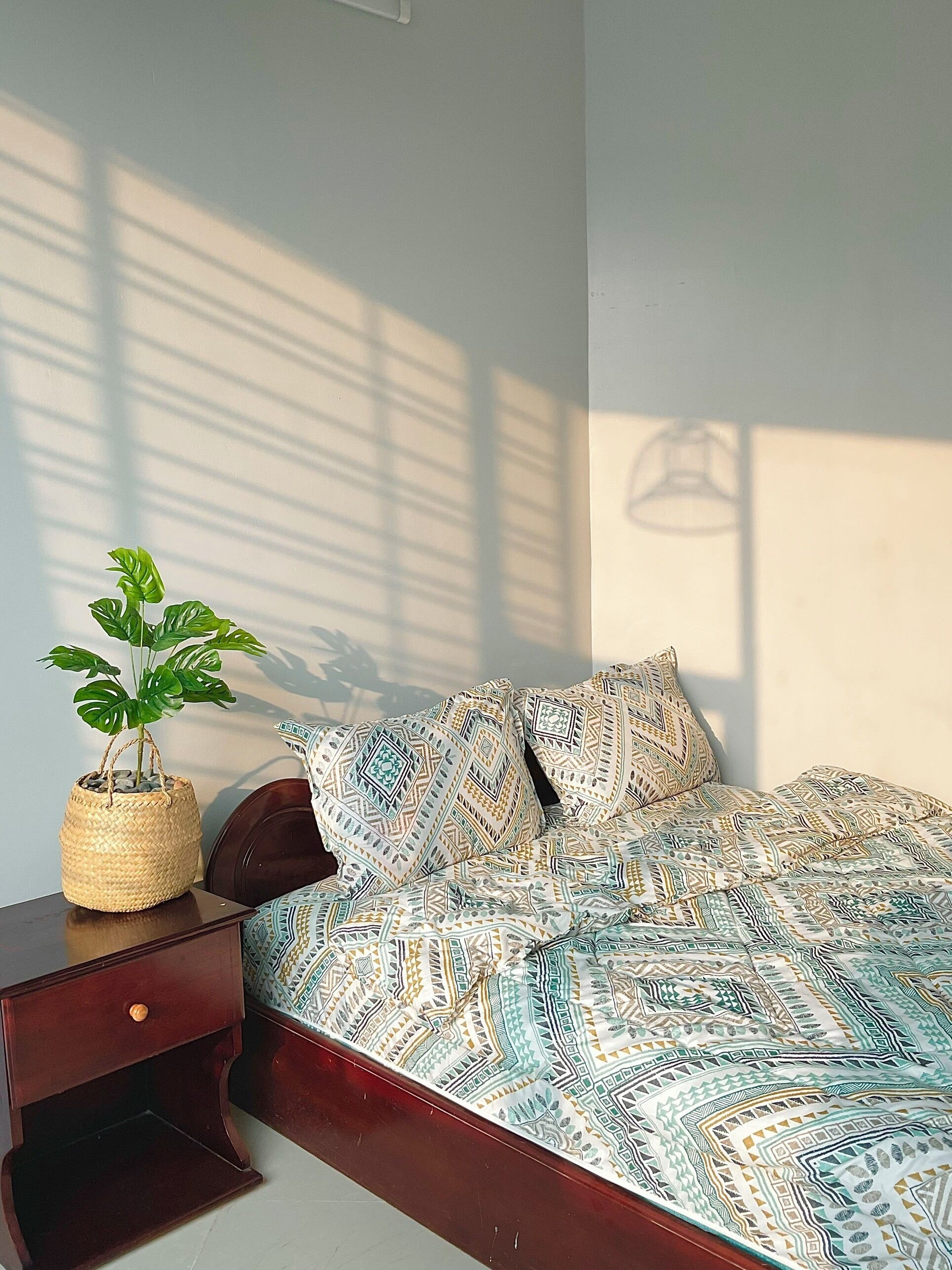 A bedroom with a bed, a nightstand, a potted plant, and a wall-mounted light fixture.