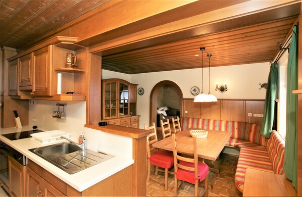 A compact kitchen with wooden cabinets, a sink, and a dining area with a bench and chairs.