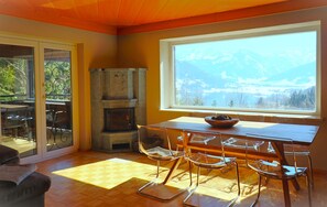 A dining area with a wooden table and clear glass chairs, a stone fireplace, and a large window with a mountain view.