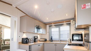 A compact kitchen with a microwave, toaster, and stove. There is a window with blinds, a sink, and a radiator.