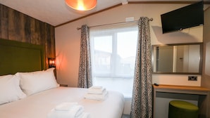 A hotel room with a bed, a desk, a mirror, and a television.