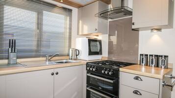 A compact kitchen with a built-in oven, a stovetop, a sink, and a window with blinds.