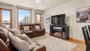 A spacious living room with a fireplace, leather sofas, and a large TV screen.
