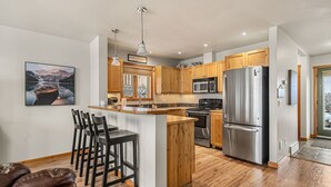 A modern kitchen with wooden cabinets, stainless steel appliances, and a bar area with stools.
