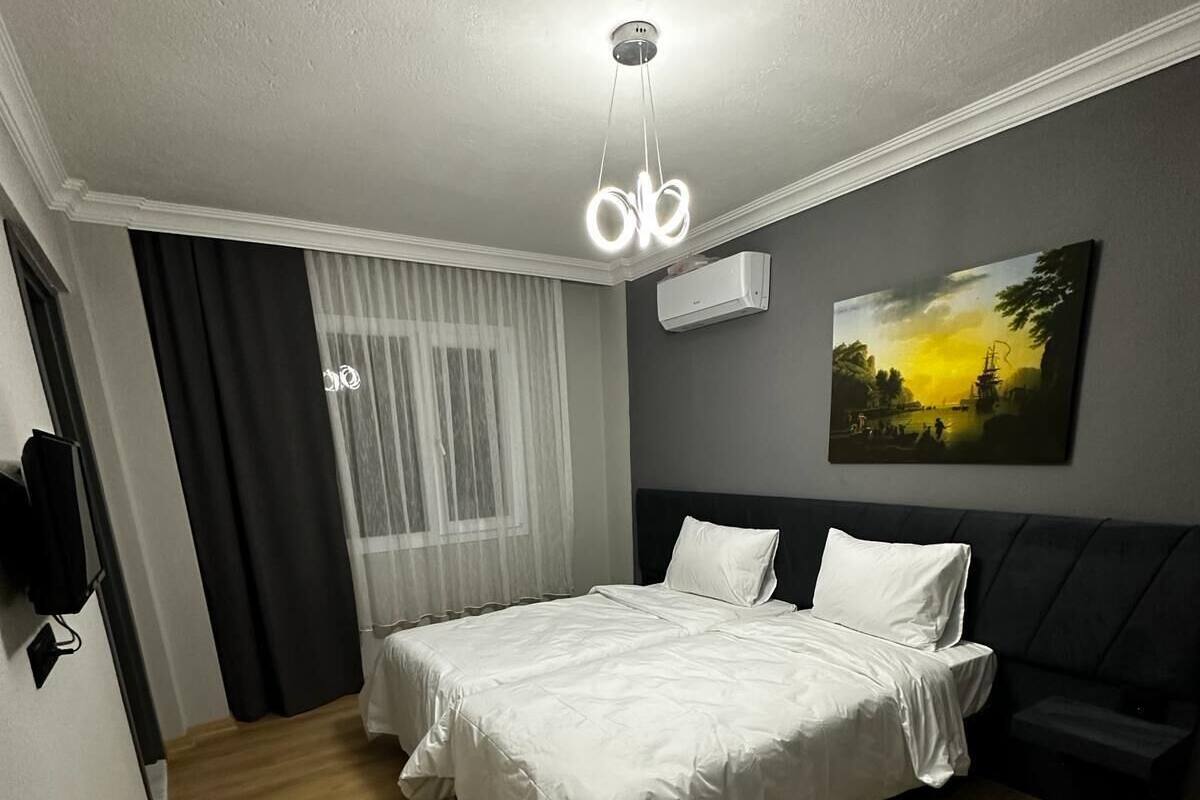 A bedroom with a bed, a bedside table, a wall-mounted air conditioner, and a painting on the wall.