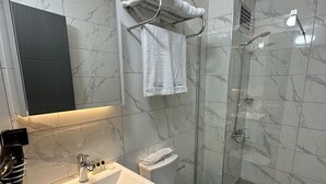 Un baño moderno con suelo de mármol, un lavabo blanco, inodoro y zona de ducha.