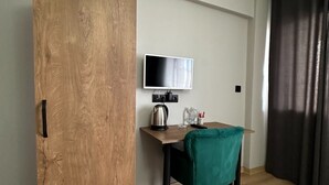 Una habitación con un armario de madera, un escritorio con televisor, una silla verde y una cortina oscura.