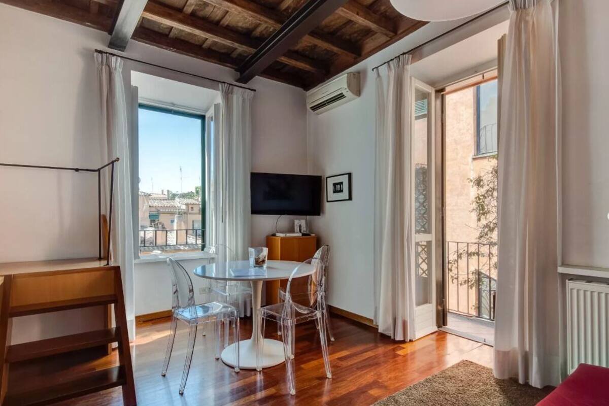 A modern living room with a wooden ceiling, a TV, a dining table with clear chairs, and a view of the city through large windows.