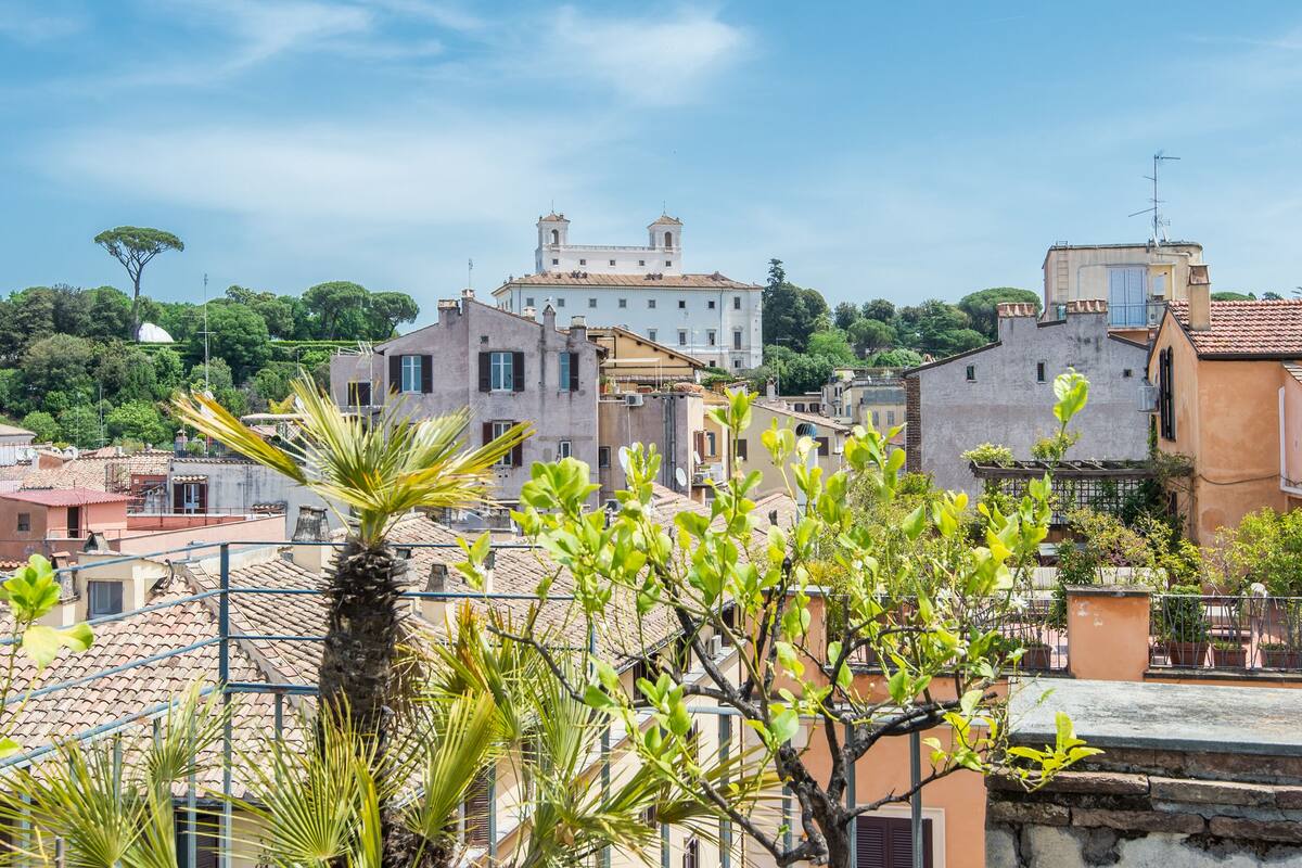 A view of a historic town with traditional architecture, including a prominent building with a bell tower, surrounded by lush greenery and residential buildings.