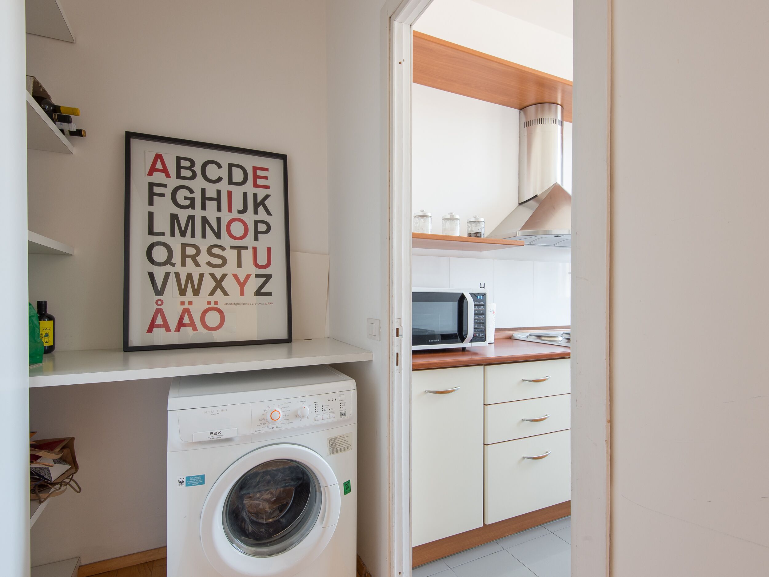 Une buanderie équipée d’un lave-linge, d’un four à micro-ondes et d’une affiche illustrant l’alphabet, accrochée au mur.