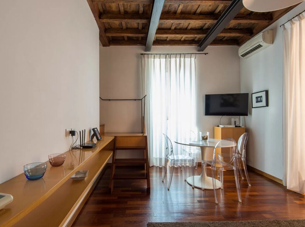 Un salon moderne avec un plafond en bois, un téléviseur à écran plat, une table à manger avec des chaises et un escalier menant à un autre niveau.