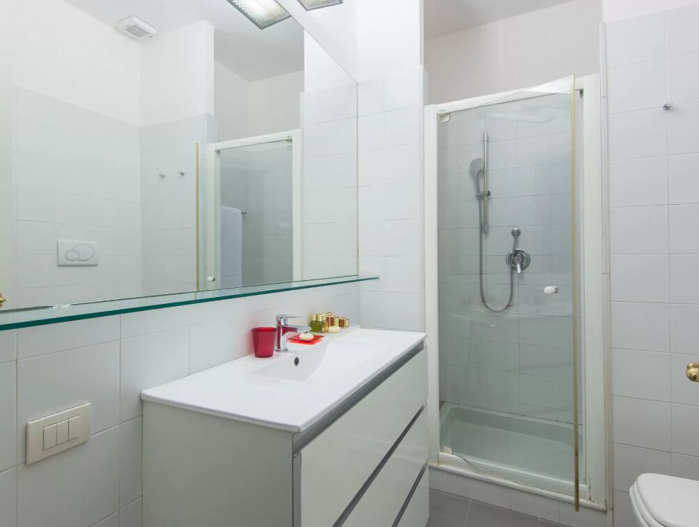 A modern bathroom with a glass shower enclosure, a white sink with a red cup, and a large mirror.