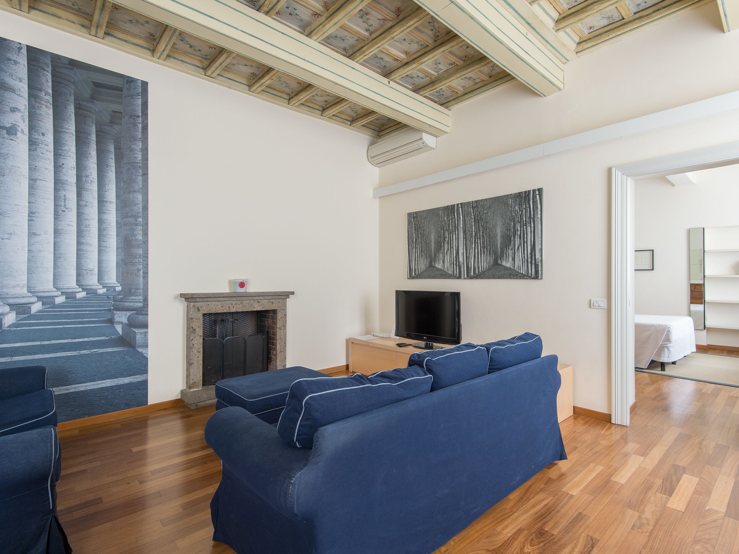 Uma sala de estar com um sofá azul, lareira, televisão e um grande quadro de colunas.