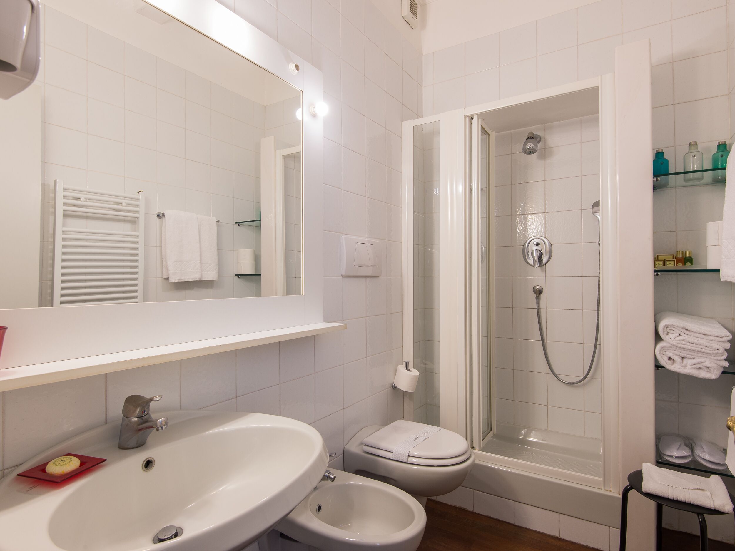 Un baño con lavamanos, bidé, inodoro y ducha con mampara de vidrio.