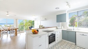 A modern kitchen with a large island, a dining area with a view, and a view of the sea. - Sunset Towers 8, 25 Donald St - heart of town with water views (Nelson Bay)
