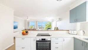 A modern kitchen with white cabinetry, a built-in oven, and a dining area with a view of the sea. - Sunset Towers 8, 25 Donald St - heart of town with water views (Nelson Bay)