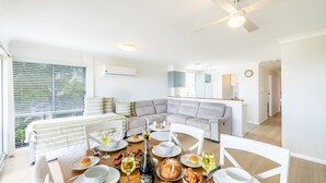 A modern living room with a sectional sofa, dining table set for a meal, and a kitchen area visible in the background. - Sunset Towers 8, 25 Donald St - heart of town with water views (Nelson Bay)