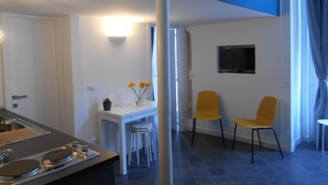 A modern kitchen with a dining area, a TV mounted on the wall, and a view of the outdoors. - Manuela Apartments San Domenico Centro Storico (Napoli)