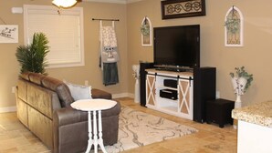 A living room with a brown leather sofa, a white side table, a ceiling fan, a flat-screen TV, and a decorative wall piece. - Spacious one bedroom 2 miles from Texas Tech!

 (Lubbock)