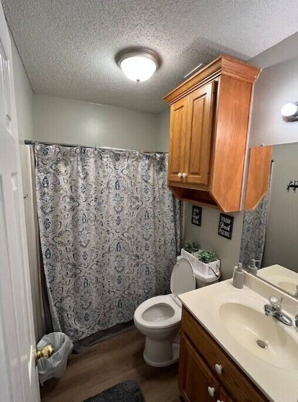 Un baño pequeño con cortina de ducha, inodoro, lavabo y armarios de madera.