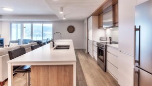 A modern kitchen with a central island, built-in appliances, and a view of the city. - Serenity by the Slopes: Tremblant Waterfront Condo (Mont-Tremblant)