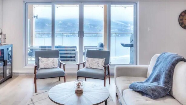 A modern living room with a sofa, two armchairs, a coffee table, and a view of a balcony with a railing. - Serenity by the Slopes: Tremblant Waterfront Condo (Mont-Tremblant)