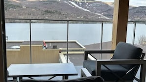 A balcony with a view of a lake and mountains. There is a table and two chairs. - Serenity by the Slopes: Tremblant Waterfront Condo (Mont-Tremblant)