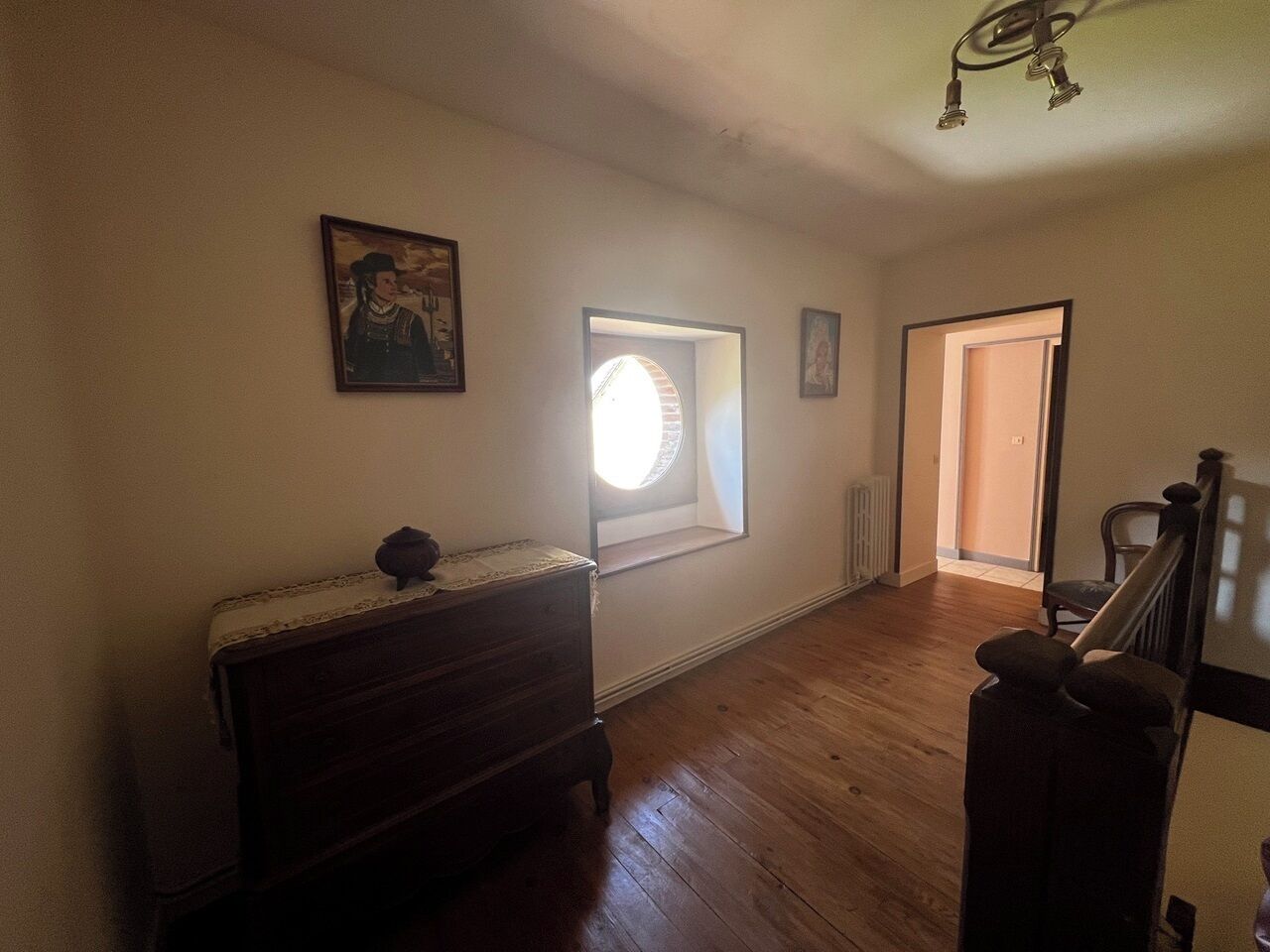 Une pièce avec une commode en bois, une fenêtre avec des stores, une porte et un escalier.