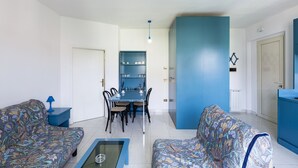A living room with patterned sofas, a glass coffee table, a dining table with chairs, and a blue accent wall. - VILL' ANDREA (App. 6) (Cecina)