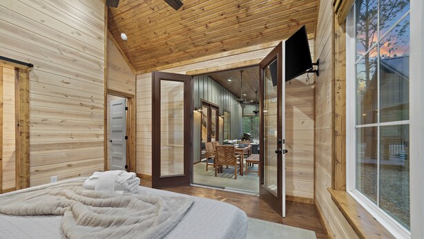 Een houten blokhut van binnen, met een bed, een eethoek en een groot raam.